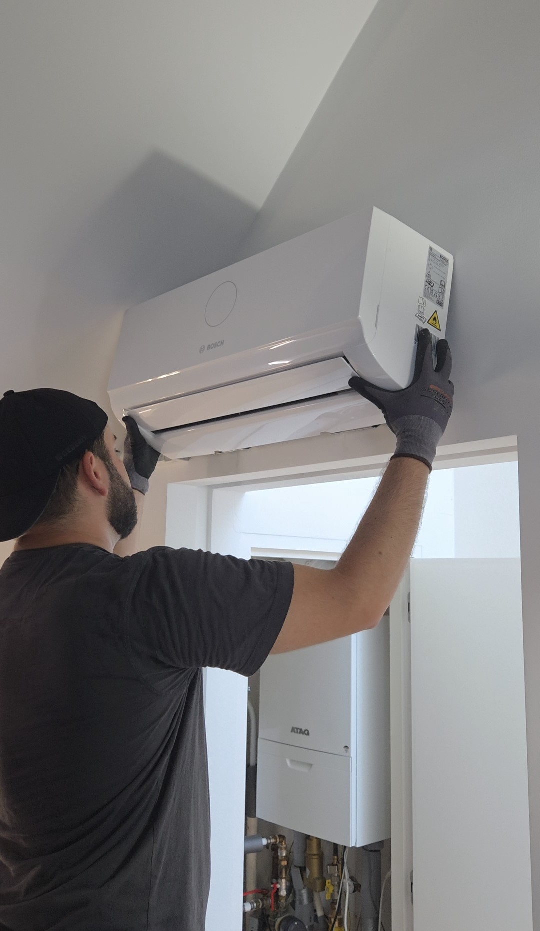 Technicien installe une unité de climatisation murale blanche, en ajustant le panneau intérieur.
